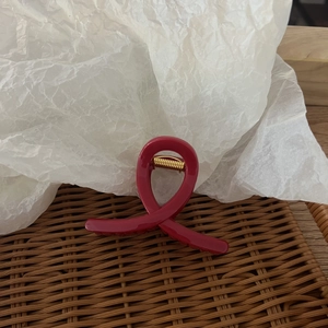 Detail of a curved red hair claw clip with a gold spring on a woven rattan tray