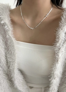 Close-up of a silver bow necklace on a collarbone with a refined polished metal finish