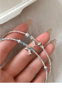 Close-up of silver fish charms and blue crystal beads on a delicate pearl bracelet