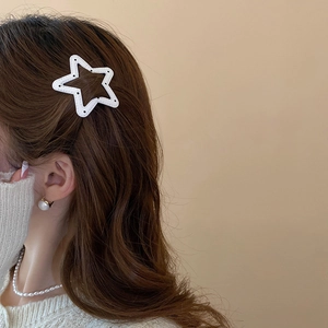 Detail shot of a white star-shaped hair clip with black dotted stitching on wavy brown hair