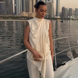 Elegant beige sleeveless halter neck draped top with high collar and urban cityscape view