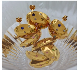 Close-up of gold semi-spherical earrings with colorful rhinestones in a glass bowl