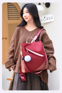 Burgundy waterproof nylon backpack with colorful straps and a white plush ball charm