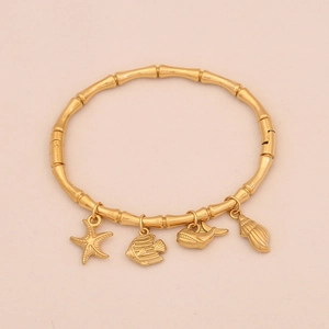 Dettaglio del bracciale dorato stile bambù con ciondoli a stella marina, balena e conchiglia