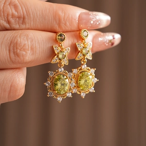 Détail de boucles d'oreilles vintage dorées avec zircon vert ovale et trèfle