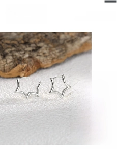 Macro shot of silver star-shaped hoop earrings on natural wood and textured surface