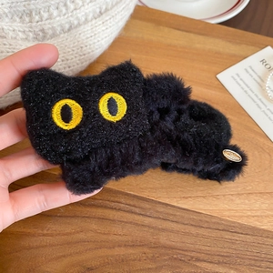 Gros plan d'une pince à cheveux chat en peluche noire avec yeux brodés jaunes et texture douce