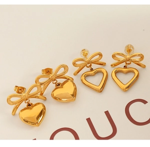 Macro detail of gold-tone bow earrings with solid and hollow heart-shaped pendants