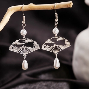 Detailed shot of fan-shaped silver tassel earrings with pearls hanging on a wooden branch