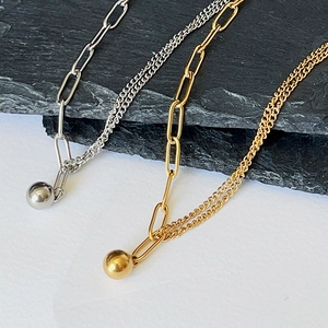 Detail of 18K gold plated asymmetric chain necklace with smooth golden ball pendant