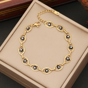 Golden stainless steel chain bracelet with enamel evil eye charms on a beige jewelry box