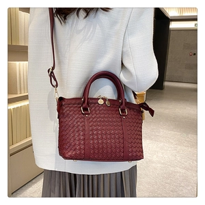 Détail du sac à main bordeaux en cuir tressé porté par un mannequin dans un décor minimaliste