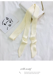 Close-up of a cream narrow silk scarf tied on a white handbag for elegant styling