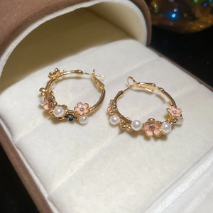 Macro detail of gold hoop earrings with pink enamel flowers and white pearls in a jewelry box