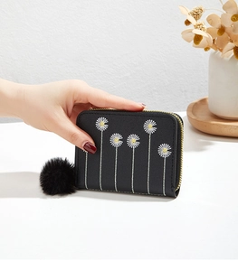 Close-up of black plush wallet with daisy embroidery, gold zipper and faux fur pompom