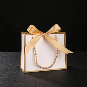 Elegant white gift bag with golden border, ribbon bow and twisted handles for wedding favors