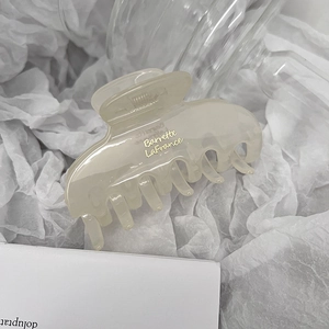 Detail of a transparent cream-colored acrylic hair claw clip with gold lettering