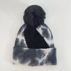 Close-up of tie-dye knit beanie with black fluffy faux fur pompom and ribbed cuff