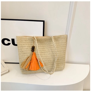 Detail of hand-woven straw tote with elegant long straps and orange tassel pendant