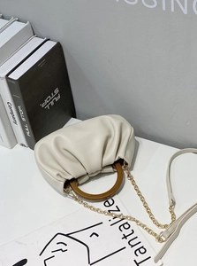Detail of a creamy white pleated cloud bag featuring a brown wooden ring handle and chain