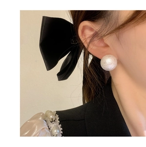 Close-up of matte silver ball stud earring worn by a model with a black bow hair clip