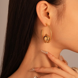 Detailed close-up of gold-plated twisted hoop earrings with a smooth metallic bead