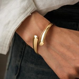 Close-up of a gold crossover open cuff bracelet featuring polished teardrop ends on a wrist