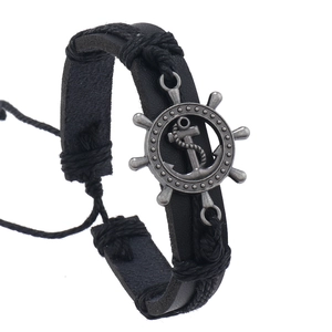 Detail view of woven black leather bracelet featuring vintage bronze anchor and helm charms