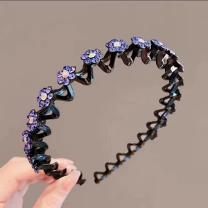 Detail showing hand holding a wavy black headband with purple rhinestone flowers