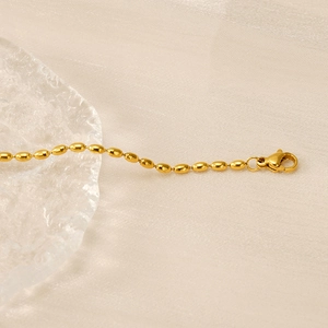 Close-up of gold-plated oval bead chain with lobster clasp on a textured fabric