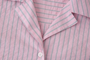 Détail du col d'une chemise en popeline à rayures roses avec texture de tissu et bouton blanc