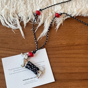 Détail du pendentif teckel en céramique avec corde tressée et perles rouges sur bois