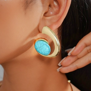 Close-up of elegant gold twisted resin earrings featuring blue turquoise stones on a model