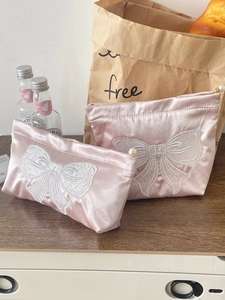 Detailed view of pink satin cosmetic bags with white bow embroidery and pearl charms