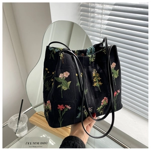 Detail view of black canvas bucket bag featuring vibrant floral embroidery and magnetic closure