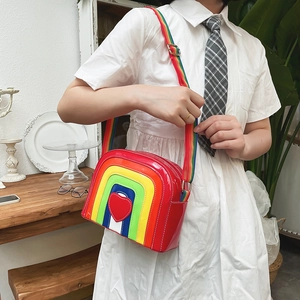 Detail of a rainbow heart crossbody bag in patent leather worn by a model in a cafe