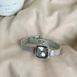Detailed close-up of a silver square watch dial with a sleek stainless steel mesh strap