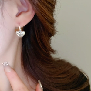 Close-up detail of a minimalist silver heart earring worn by a model in soft lighting