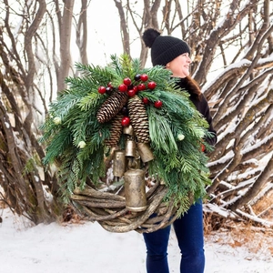 Rustic Christmas wreath with pine cones and bronze bells held in a snowy forest setting