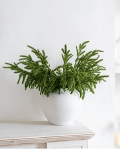 Realistic green cedar branches in white ceramic vase on a minimalist fireplace mantle
