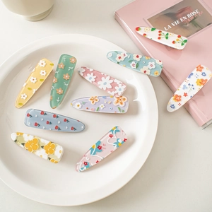 Close-up of nine acrylic flower hair clips with colorful floral patterns on a white plate