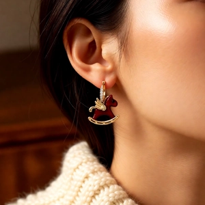 Detailed close-up of a zircon-inlaid horse earring with golden wing and deep red finish