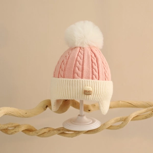 Close-up of pink knit baby hat with CHOCO patch, twist pattern, and white pompom