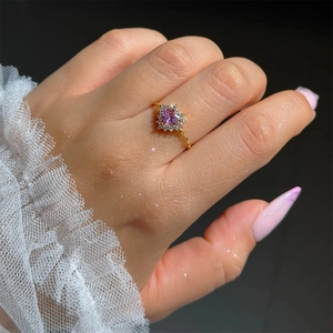 Detail of a gold pull-chain ring featuring a pink heart stone and surrounding diamonds