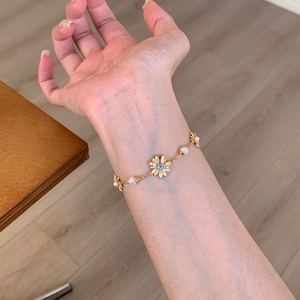 Detailed view of a dainty gold daisy bracelet with pearls and blue zircon center