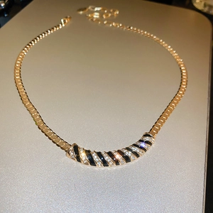 Macro detail of gold snake chain with black enamel and rhinestone striped pendant