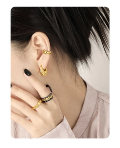 Close-up of minimalist gold geometric earrings and textured rings on model's ear and hand