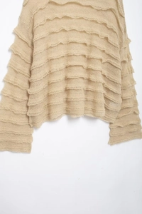 Detail of beige knit sweater featuring layered ruffle edges and translucent woven texture