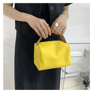 Detail of a small yellow candy-colored crossbody bag with a wide beige handle