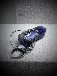Detailed view of silver claw-shaped amethyst pendant on dark stone background
